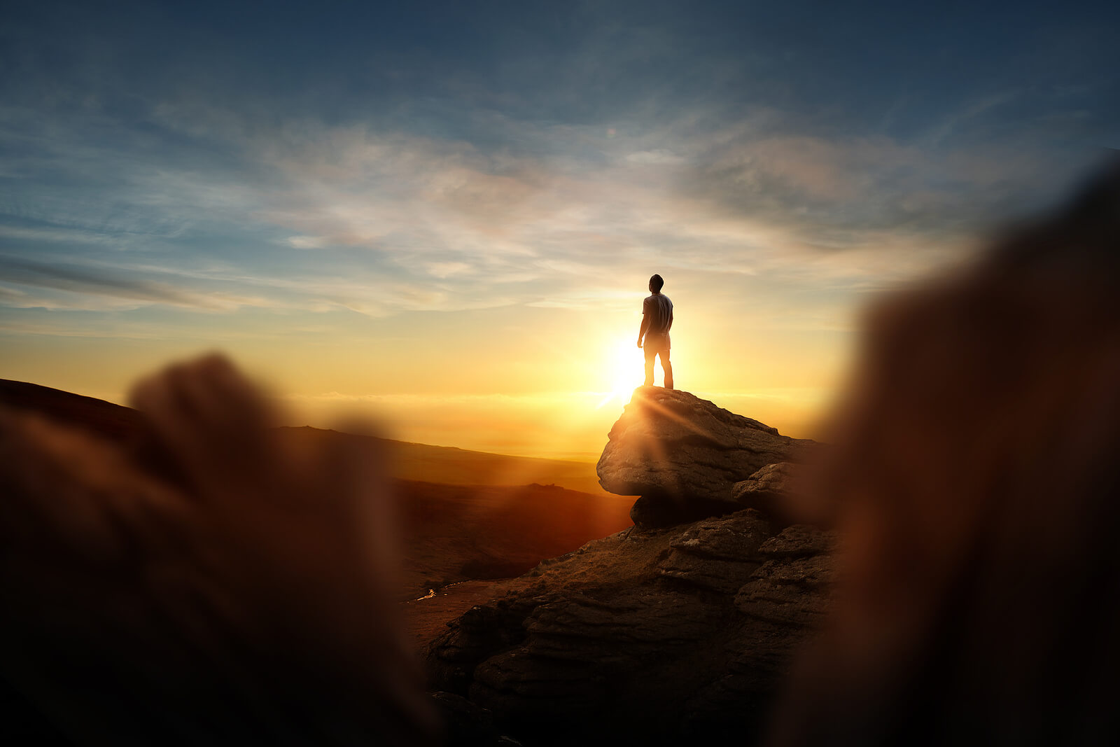 A person stands atop a rock while looking out over the morning landscape. This could represent the hope life transitions therapy in Seattle, WA can help cultivate. Learn more about online life transitions therapy in Seattle, WA by contacting an online therapist in Seattle, WA today.