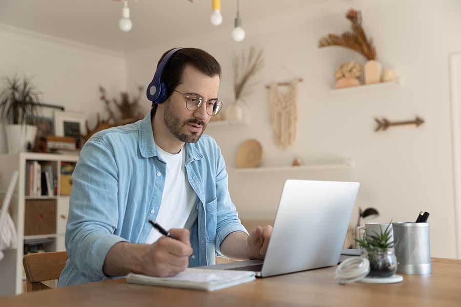 A man takes notes while listening to something on his laptop. Learn how online therapy in Washington can support you from the comfort of home. Contact an online therapist in Seattle, WA for support with online therapy for depression and other services.