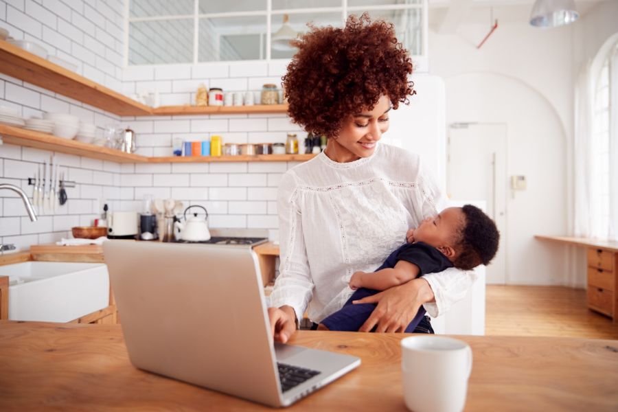 A mother smiles while holding her baby and typing on a laptop. This could represent searching for an anxiety therapist in Seattle, WA online. Learn more about online therapy for anxiety in Seattle, WA and the support anxiety treatment in Seattle, WA can offer. 