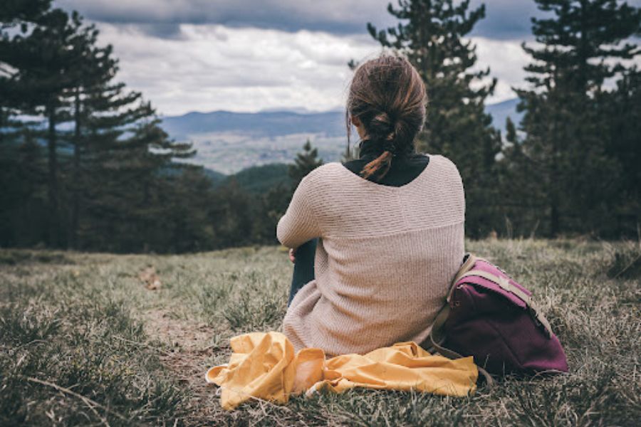 A woman sits alone on a trail overlooking the valley below. This could represent the isolation a life transitions therapist in Seattle, WA can offer support with overcoming. An online therapist in Seattle, WA can offer support from the comfort of home with remote life coaching in Seattle, WA and other services.