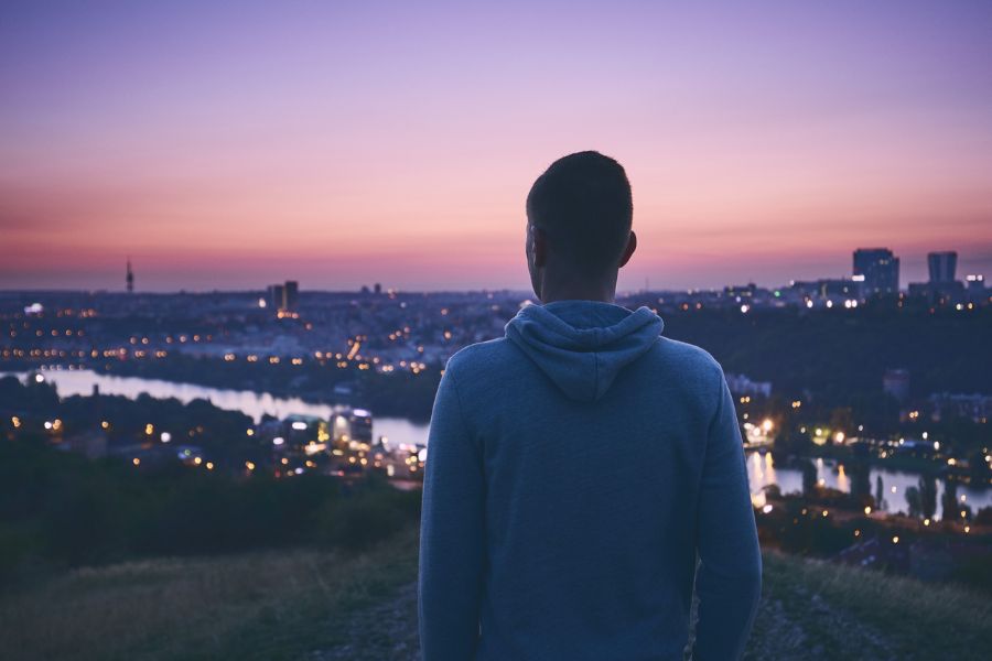 A person in a hoodie looks out at a cityscape in the evening. This could represent the isolation of trauma that EMDR therapy in Seattle, WA can help you overcome. Contact an EMDR therapist in Seattle, WA to learn more about the benefits of online EMDR therapy in Seattle, WA, and across the state. 