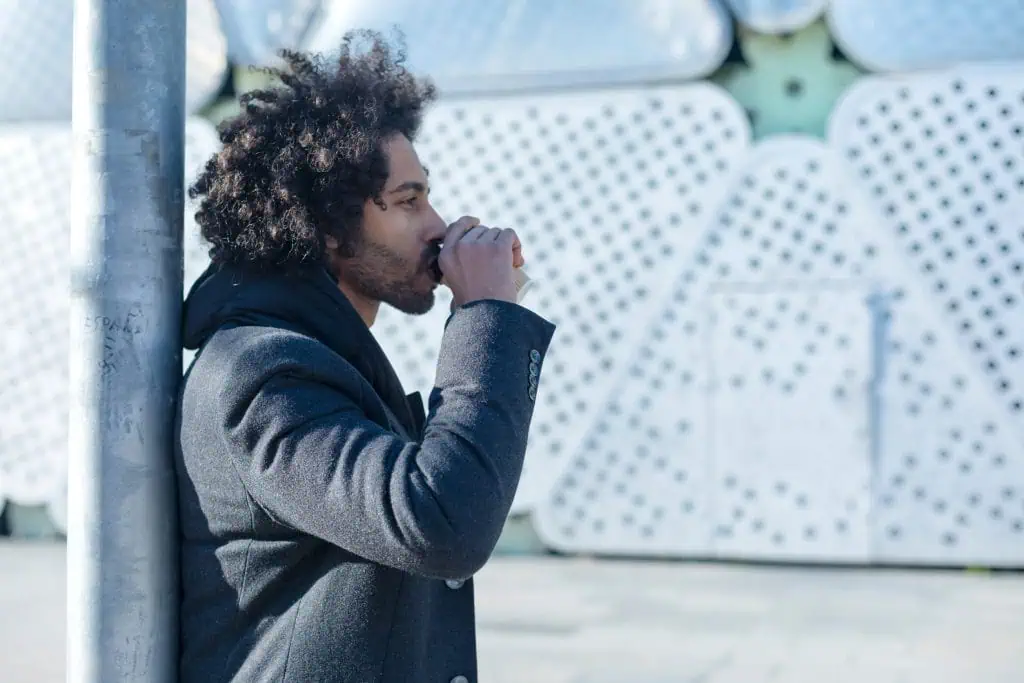 Side view of a man standing and drinking a takeaway coffee, reflecting on how they are dealing with their emotions 