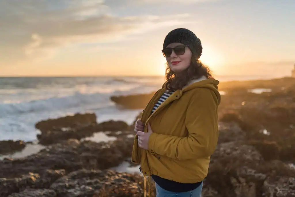 Young woman posing in front of sunset. Walking along seaside in the fall.
