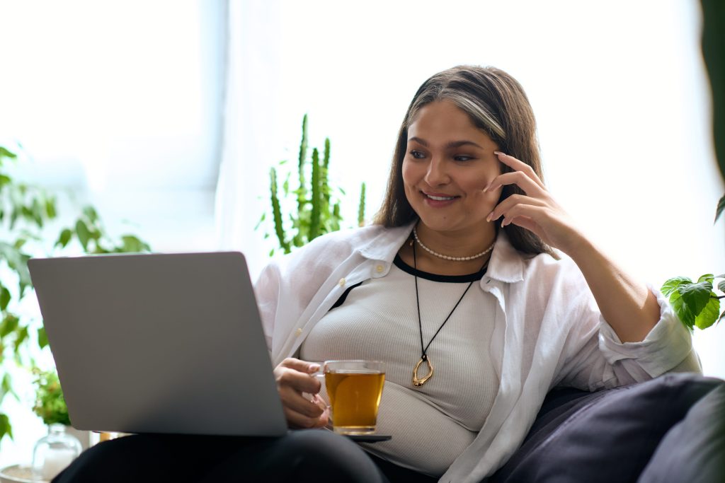 woman sitting at home with her computer on her lap engaging in online therapy for shame in Seattle, WA