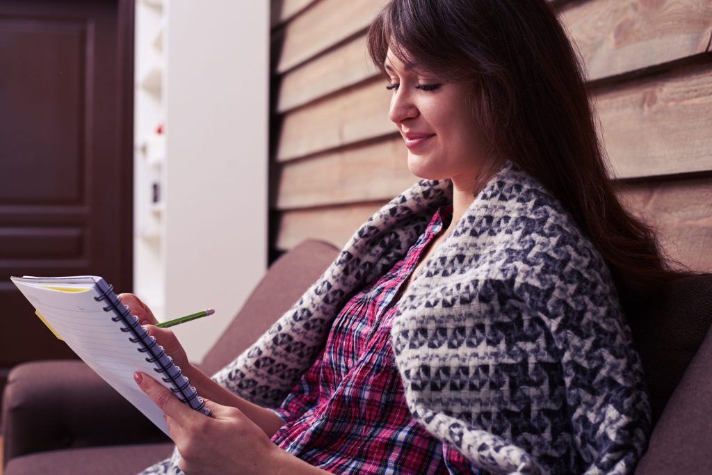 Side view of woman with notebook sitting on the sofa engaging in coping skills.
