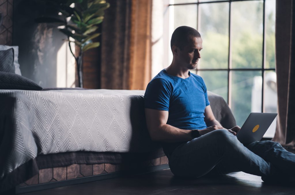 Adult man in blue t-shirt on laptop engaging in online therapy 