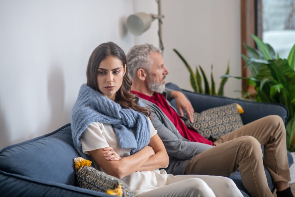 A young woman and her dad sitting on a sofa in conflict