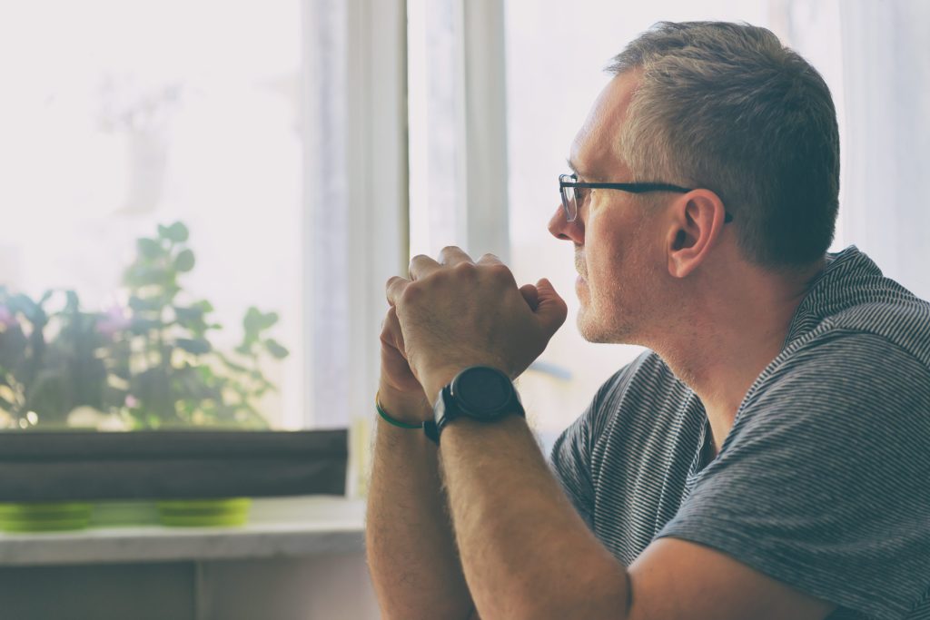 Man is sitting in the living room at the table in deep thought.